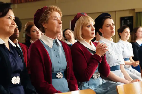 Linda Bassett as Nurse Crane and Helen George as Trixie Aylward, sitting in a crowd, looking up at a stage while listening to someone speak
