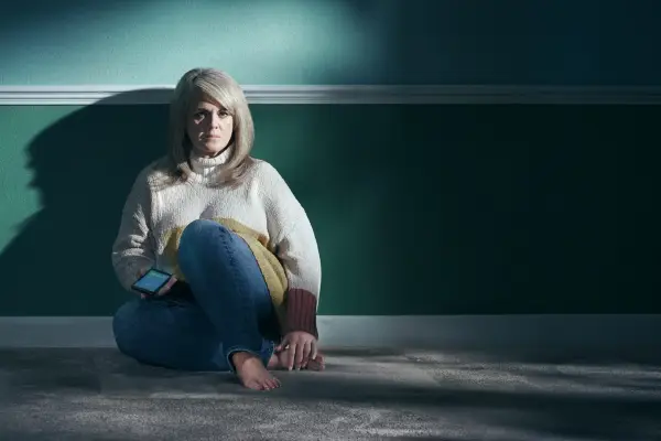 Sally Lindsay in Cold Call, sat on the floor against a wall