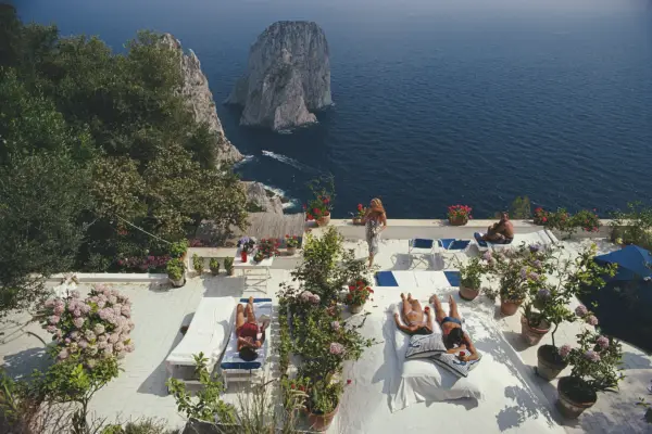 Sunbathers lounge on the white-painted terrace of Il Canille, built into the rocks of Pizzolungo overlooking the waters off the coast of the island of Capri, Italy, in August 1980. Il Canille is the villa owned by Italian tailor and fashion designer Umberto Tirelli (1928-1992). (Photo by Slim Aarons/Getty Images)