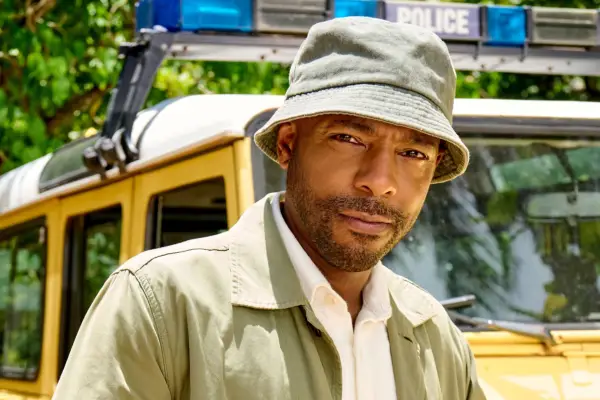 Don Gilet as DI Mervin Wilson, looking ahead with a white shirt and green jacket and hat.