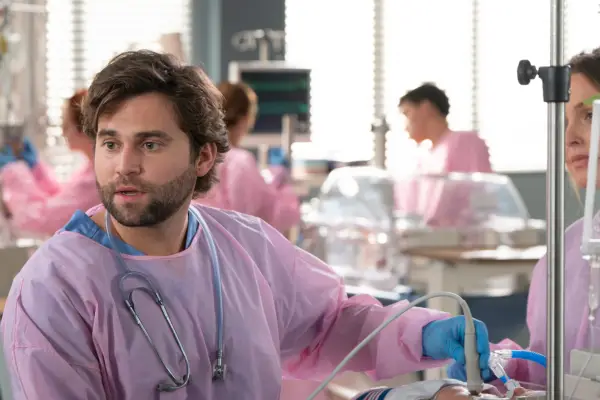 Jake Borelli as Dr Levi Schmitt in pink scrubs treating a baby in Grey