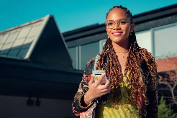 Elle smiles while holding her phone as the sun shines on her