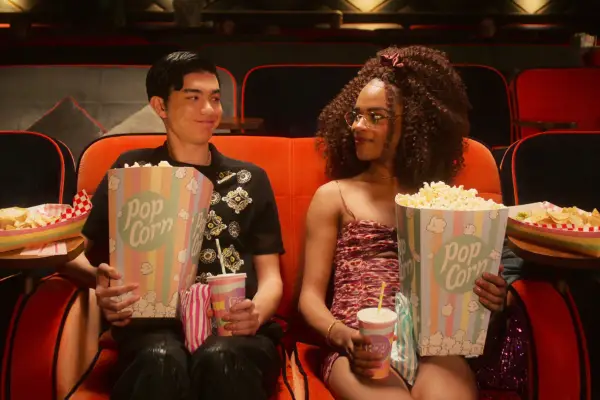 Will Gao and Yasmin Finney sitting in a cinema seat, holding popcorn and looking at each other