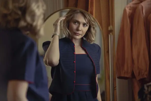 Elizabeth Olsen plays Candy Montgomery in Love & Death, wearing a navy outfit, looking in a mirror