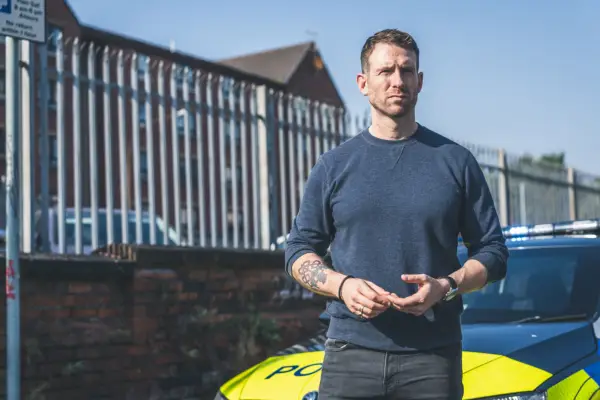 Craig McGinlay as Craig in Blue Lights, stood in front of a police car