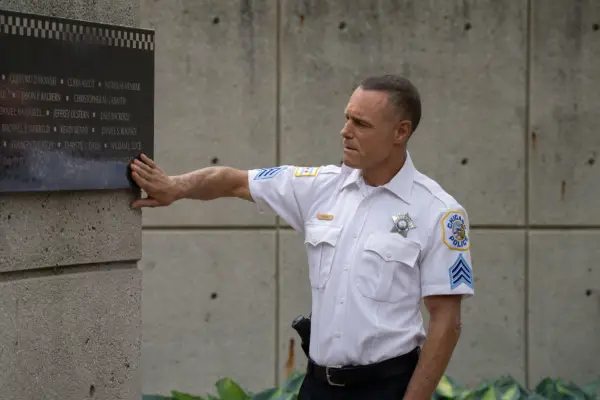 Jason Beghe as Hank Voight in Chicago PD season 13 wearing his uniform, putting his hand on a memorial sign.