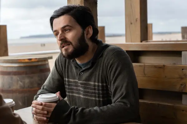 Elham Ehsas as Asif Syed in Unforgotten season 6 sitting in a cafe holding a cup and speaking to someone.