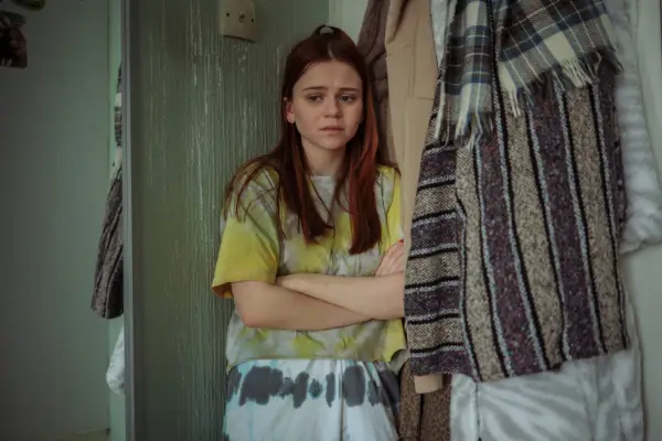 Matilda Freeman as Lilly Wells standing in the corner of her bedroom with her arms crossed and looking scared in Passenger.