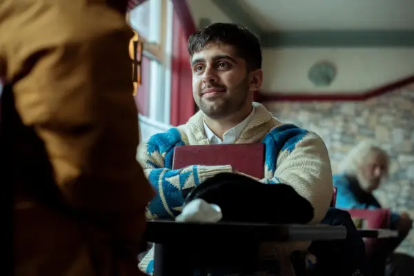 Arian Nik as Nish Chowdry looking happy and smiling as he holds a folder to his chest in Passenger.