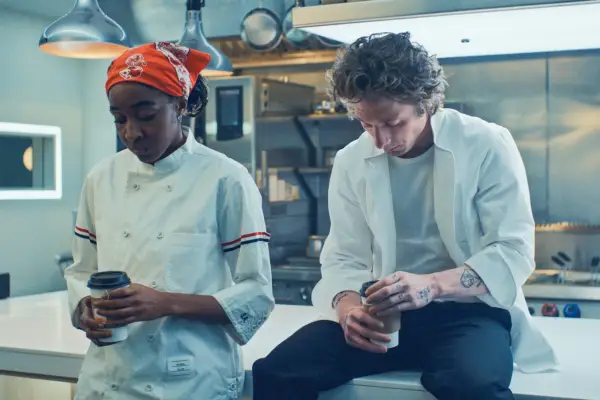 Jeremy Allen White as Carmy and Ayo Edebiri as Sydney in The Bear season 3. He is sat on a restaurant countertop and she is leaning against it.