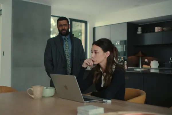 Michelle Keegan as Maya and Adeel Akhtar as DS Sami Kierce, Maya sitting at the table staring at a laptop with Kierce standing next to her.