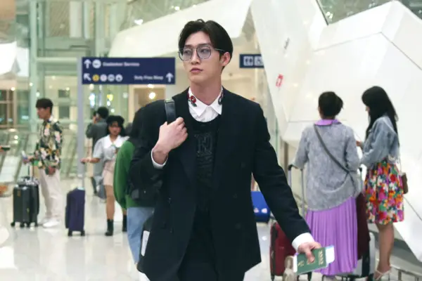 Min Ho walking at the airport with his passport in one hand and wheeling his case