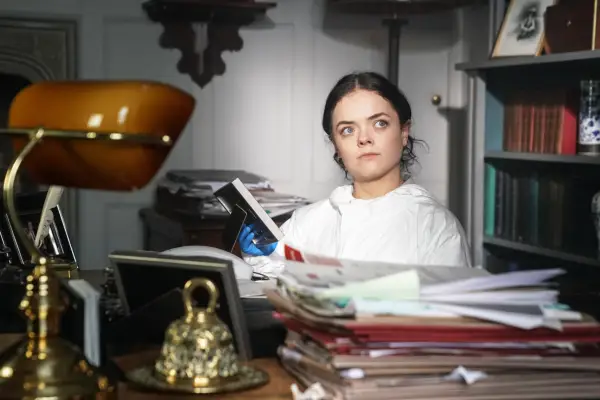 Francesca Mills plays Kit Brooks, wearing white, sat in a wheelchair at her desk