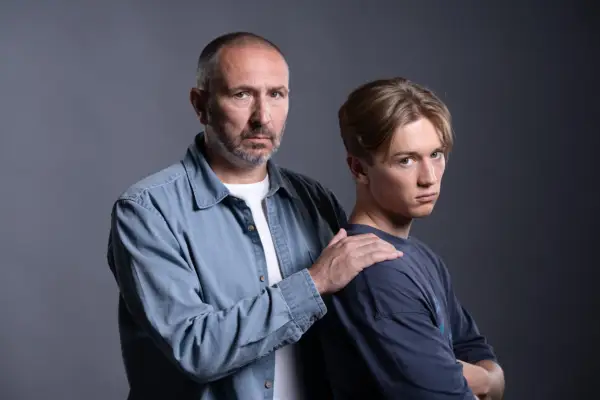 Alex Walkinshaw as Ross Marshall with his hand on the shoulder of Max Murray as Joel Marshall against a grey background in EastEnders.