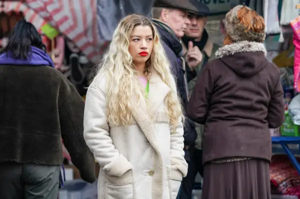 Molly Rainford as a sullen Anna Knight in an off-white coat standing on a busy street in EastEnders.