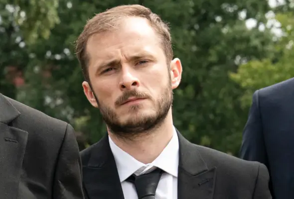 Max Bowden as Ben Mitchell with facial hair and in a suit with black tie for EastEnders.