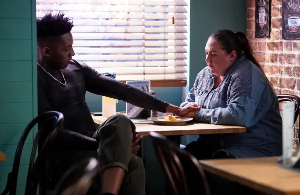 Matthew James Morrison as Felix Baker and Clair Norris as Bernadette Taylor sitting at a table in the cafe, with his hand on hers.