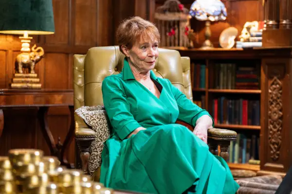 Celia Imrie sat down in a chair wearing a green dress, smiling.
