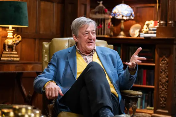 Stephen Fry sat down in a chair, smiling as he talks.