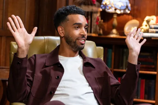 Niko Omilana wearing a white t-shirt and maroon coloured jacket.