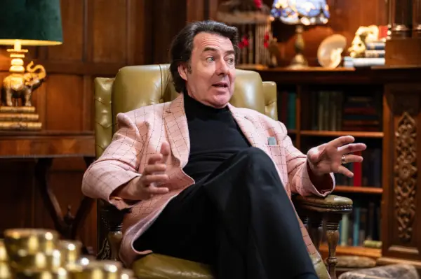 Jonathan Ross sat back in a chair, wearing a black t-shirt and a pink blazer.