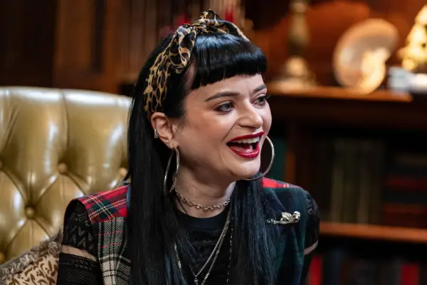Woman with dark hair, red lipstick and large hoop earrings laughs whilst in conversation with someone not pictured.