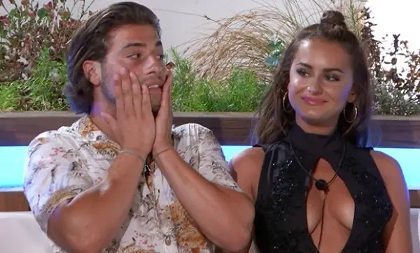 Kem and Amber sat next to each other, wearing evening clothing. Amber is smiling while looking across at something while Kem has his hands on his face.