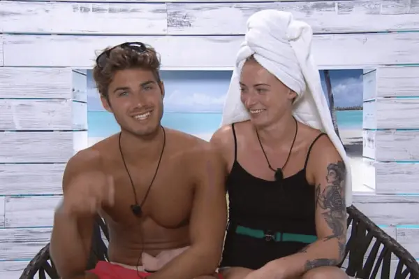 Josh Ritchie and Hannah Richardson on Love Island season 1. Lauren has a towel on her head and is looking at Josh while smiling. Josh is smiling straight on with a pair of sunglasses on his head