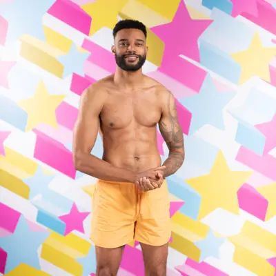 Tyler Cruickshank posing in front of a star background. He is holding his hands together and is wearing orange shorts