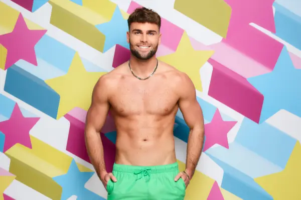 Tom Clare topless, wearing a pair of pastel green swimming shorts while posing in front of a printed star backdrop.
