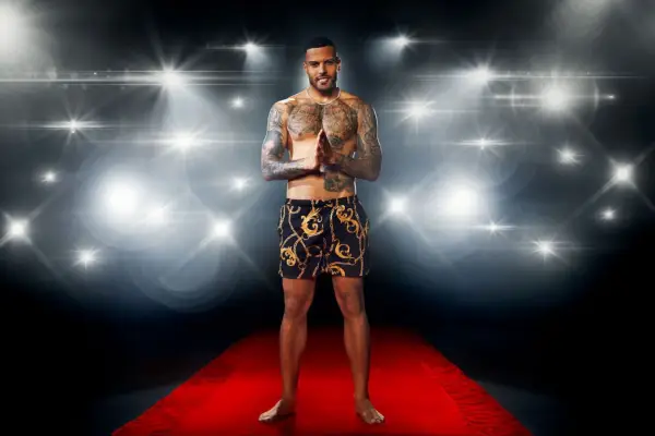 Luis Morrison posing on a red carpet in front of a flashing camera backdrop while wearing a pair of printed swimming trunks for Love Island: All Stars.