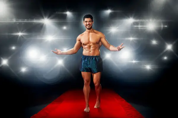 Anton Danyluk posing on a red carpet in front of a flashing camera backdrop while wearing a pair of metallic swimming trunks.