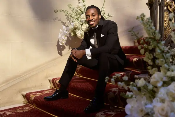 Divarni wearing a black tuxedo smiling as he stands on a set of stairs.