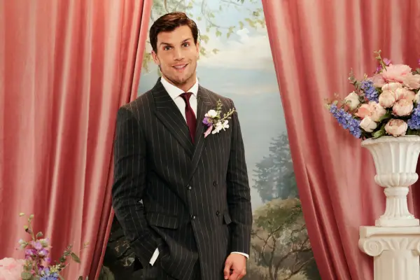 Reiss wearing a black striped blazer, smiling ahead with one hand in his pocket.