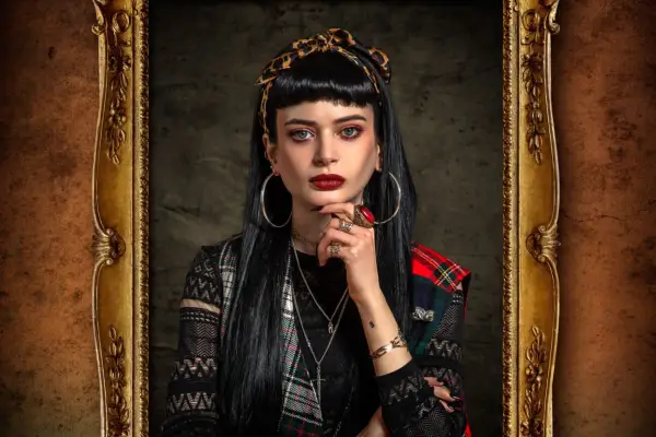 Woman with dark hair, red lipstick and large hoop earrings stares into the camera with one hand placed on her chin.