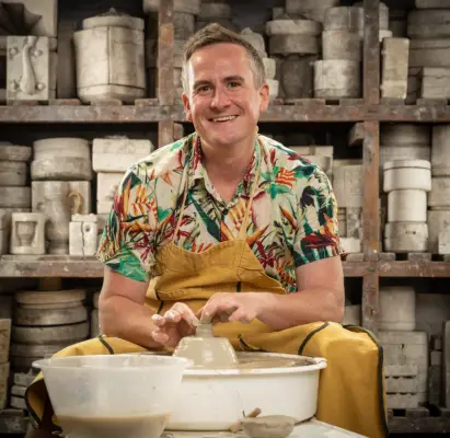 Dan wearing a multi-coloured t-shirt and brown apron doing pottery