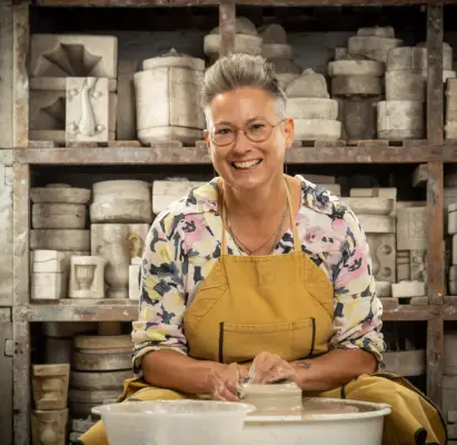 Cadi wearing a floral jumper and brown apron doing pottery