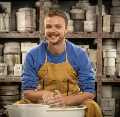 Steven wearing a blue jumper and brown apron doing pottery