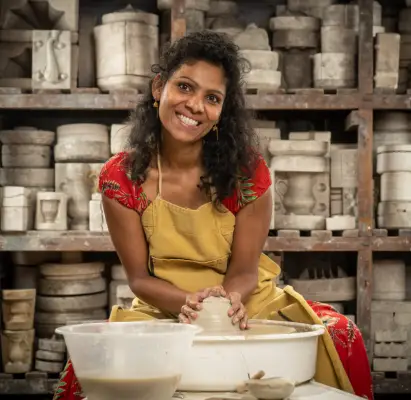 Shani wearing a red t-shirt and brown apron doing pottery