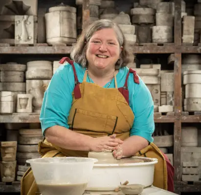 Jan wearing a blue jumper and brown apron doing pottery
