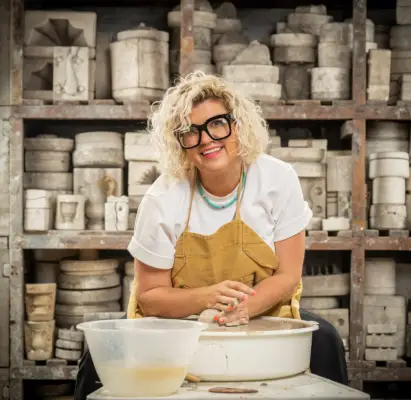 Donna wearing a white t-shirt and brown apron doing pottery