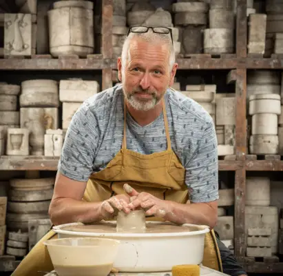 Dave wearing a grey t-shirt and brown apron doing pottery