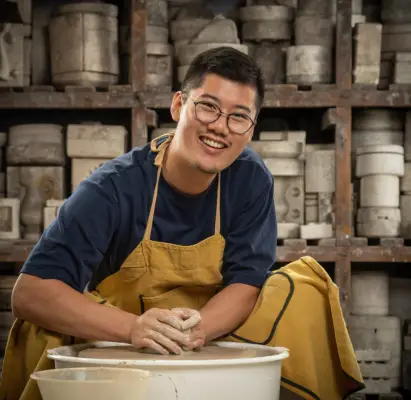 Daniel wearing a blue long-sleeved top and brown apron doing pottery