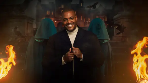 Miles for The Traitors season 2. Miles is wearing a black blazer and white turtleneck as he smiles