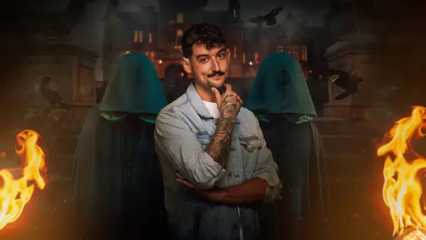 Jonny for The Traitors season 2. He is wearing a blue jacket and white t-shirt with his arms crossed