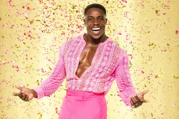 Harry Aikines-Aryeetey wearing a pink shirt that is unbuttoned matched with hot pink trousers, smiling ahead.