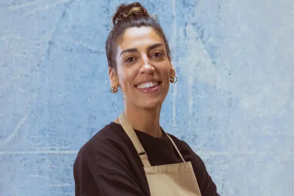 Jessika wearing a black top and a light brown apron. She is smiling ahead with her body slightly turned to the side.