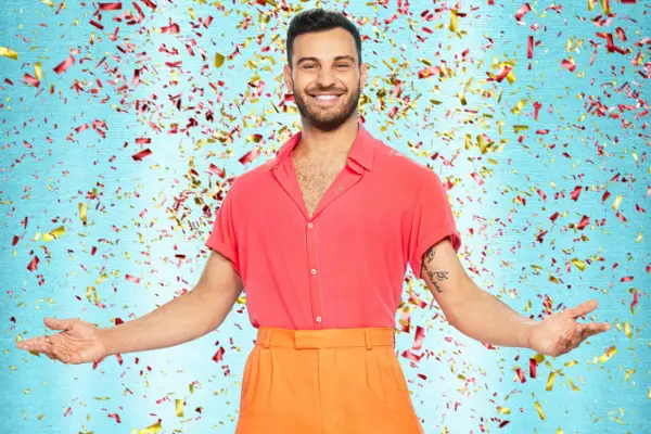 Vito Coppola wearing a pink shirt and orange trousers, smiling ahead.