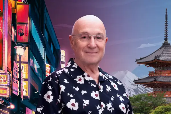 Pensioner with bald head and glasses smiles at camera with scene of Japan behind him.