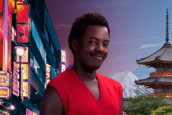 Man with brown hair and moustache wearing a red v-neck vest smiles at camera with scene of Japan behind him.